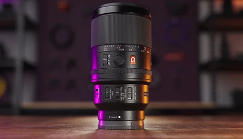 Camera lens with focus ring and aperture markings, lit by magenta and orange accent lighting against blurred background.