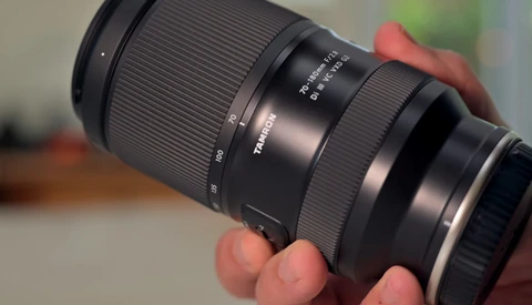 Telephoto zoom lens held in hands, showing focus and aperture rings with distance scale markings.