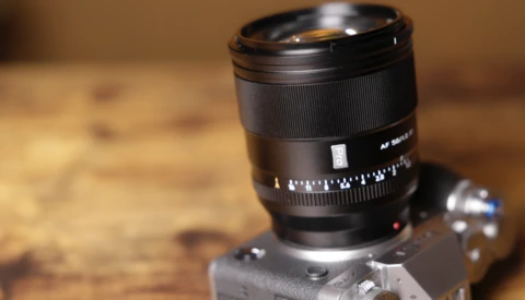 Telephoto lens mounted on vintage rangefinder camera body against wooden surface.
