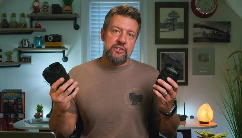 Man holding two camera bodies while discussing photography equipment in a home studio setting.