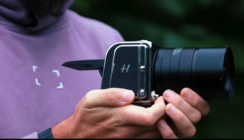 Photographer holding a medium format film camera with telephoto lens attachment.