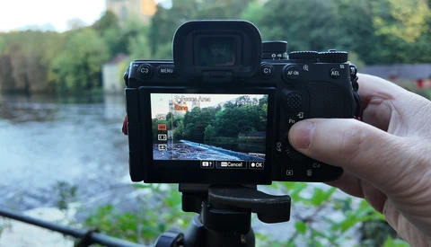 Mirrorless camera mounted on a tripod displaying a river landscape on its rear LCD screen.