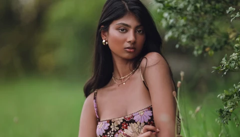 Woman in floral dress posing against blurred green foliage background.
