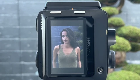 Medium format camera displaying a portrait of a woman on its rear LCD screen in outdoor daylight.