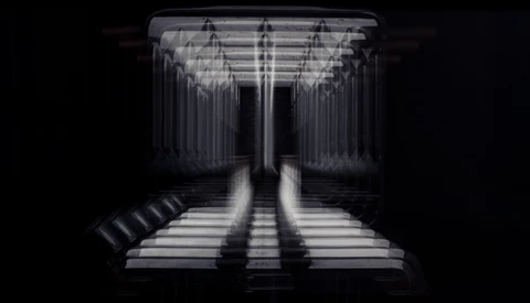 Symmetrical corridor with rows of vertical elements converging toward a vanishing point, lit with dramatic side-lighting creating strong linear shadows.