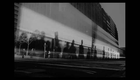 Blurred figures walking past a modern building with horizontal bands of light and dark surfaces.