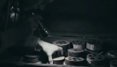 Film reels and storage containers arranged on a surface in dramatic low-key lighting.