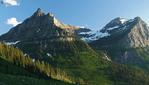 Mountain peaks with snow patches and dense evergreen forest in valley below under clear sky.