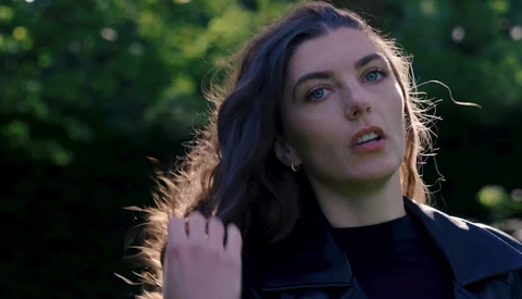 Woman with dark hair looking upward in golden hour sunlight against blurred green foliage.