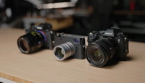 Three mirrorless cameras arranged on a wooden table, displaying different lens and body configurations.