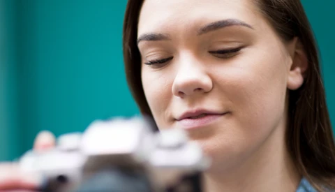 Woman with eyes closed against turquoise background, with blurred camera equipment visible behind her.