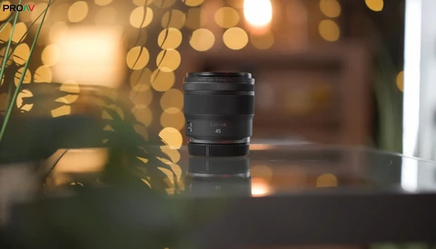 Black camera lens displayed on a surface with warm bokeh lights and foliage in the background.
