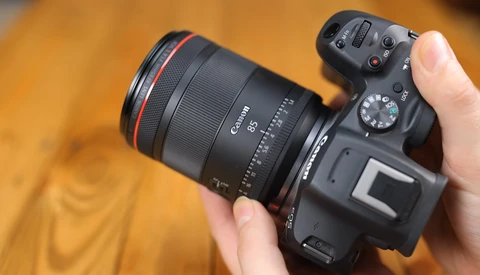 Canon mirrorless camera with RF-mount lens held in hand against warm wooden background.
