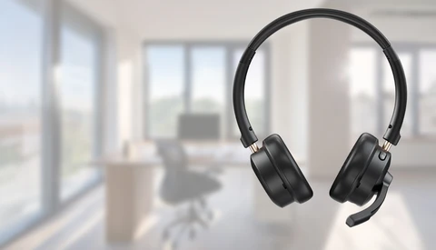 Black over-ear headphones suspended against a blurred modern office interior with windows and furniture.