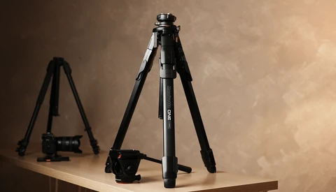 Professional tripod with ball head and video camera on wooden surface against warm backdrop.
