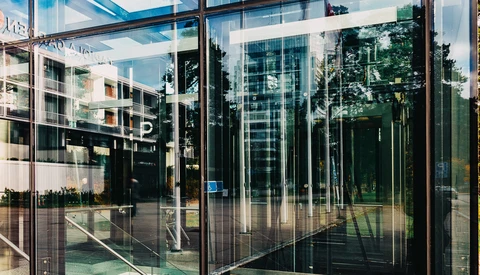 Modern glass storefront with reflections of surrounding buildings and trees on transparent panels.