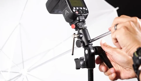 Photographer adjusting a flash unit mounted on a light stand with white umbrella diffuser.