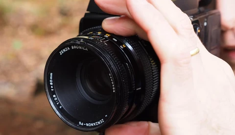 Hands holding a Zenza Bronica medium format camera lens in outdoor daylight.