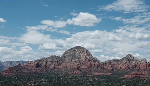 Desert mountain range with red rock formations beneath a partly cloudy blue sky.