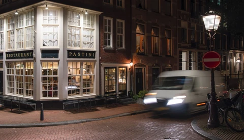 Historic European street at night with illuminated storefront and moving vehicle with motion blur.
