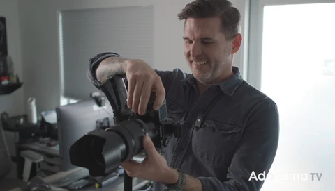 Photographer holding a professional cinema camera with a large lens attachment in a bright studio setting.