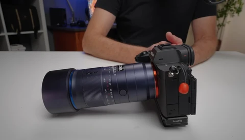 Camera with telephoto lens attached, displayed on white table with person in black shirt behind it.