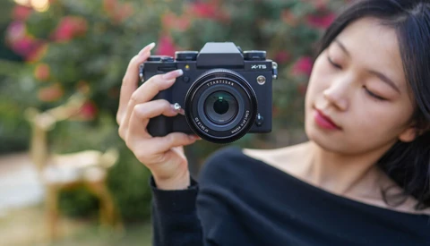 Young woman holding a mirrorless camera with a telephoto lens, looking down at the viewfinder.