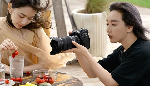 Food photographer captures a styled arrangement of fresh produce and strawberries using a professional DSLR camera.
