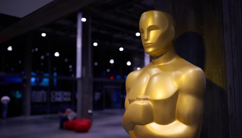 Golden Oscar statue in profile against blurred evening venue lighting.