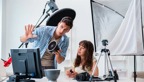 Two photographers in a studio setting with professional lighting equipment and cameras on a desk.