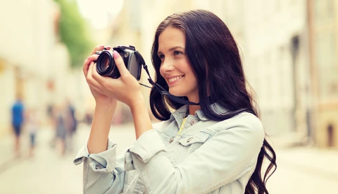 Woman holding binoculars up to her eyes while smiling at the camera on an urban street.