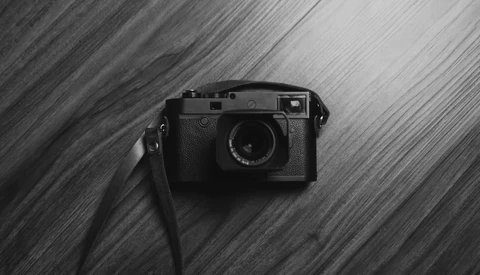 Rangefinder camera with attached strap positioned on diagonal striped wooden surface.