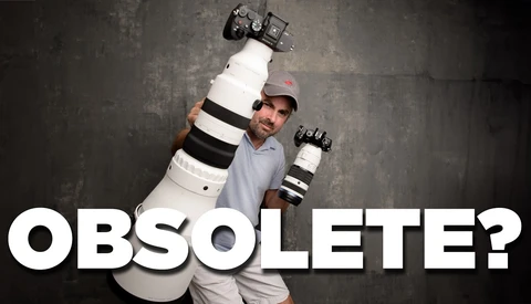 Photographer holding large telephoto lens and camera body overhead against textured gray background.