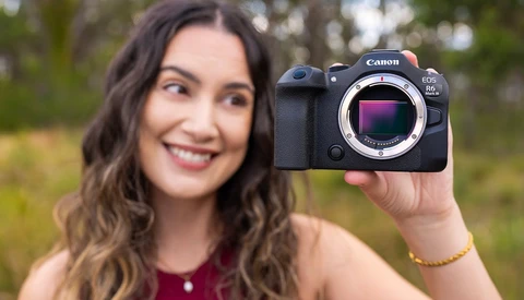 Woman holding Canon EOS R5 mirrorless camera body with sensor visible in outdoor setting.
