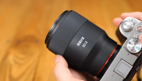 Metus 85mm lens mounted on a mirrorless camera, held in someone's hand against a warm, blurred background.