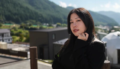 Woman in black clothing posed on a rooftop overlooking a forested valley and distant mountains.