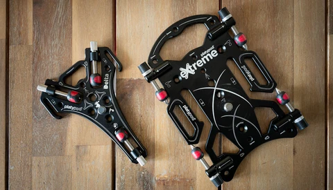 Two black mechanical disc brakes displayed on a wooden surface, showing different sizes and components.