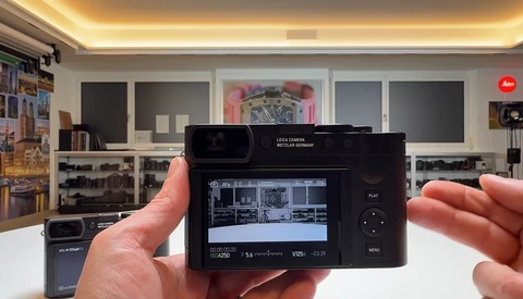 Hands holding a Leica Q camera displaying its rear LCD screen in a photography studio setting.