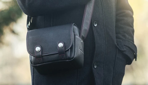 Black leather shoulder bag with metal snap buttons worn over dark jacket.