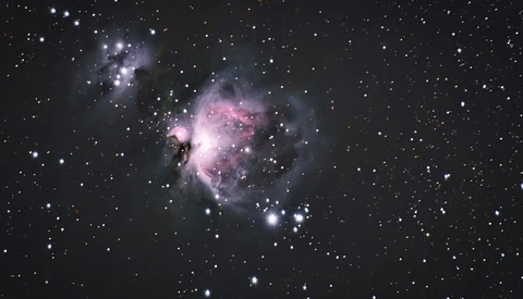 The Orion Nebula glowing pink and white against a starfield, with dark dust lanes and bright central stars.