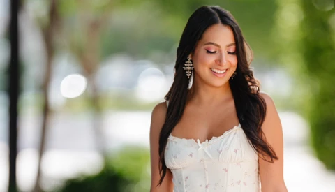 Woman in white sleeveless top looking downward with soft natural lighting in outdoor setting.