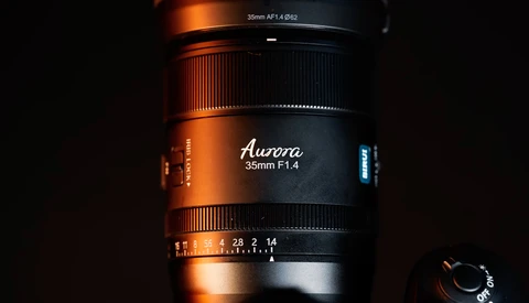 Aurora 35mm F1.4 lens with focus and aperture rings visible against dark background with dramatic orange and blue lighting.