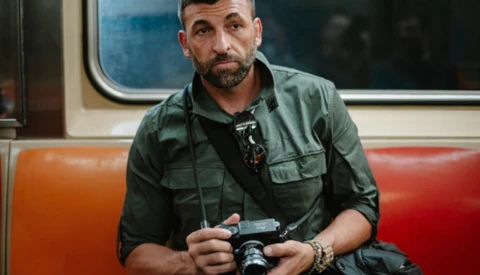 Man holding a vintage camera on public transit, wearing a green utility shirt.