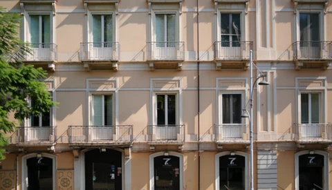 Neoclassical building facade with five stories, symmetrical windows with balconies, and dark storefronts on ground level.