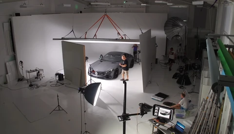Professional car photography studio setup with luxury sedan, overhead softbox lighting, and crew monitoring shoot.