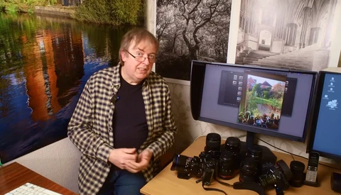 Photographer reviewing images on a monitor surrounded by camera equipment and lenses.