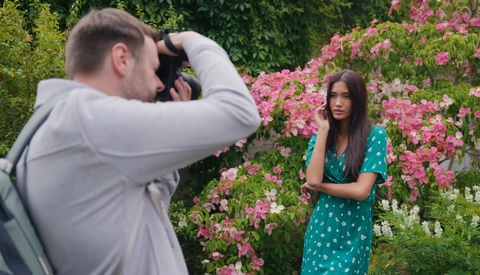 Photographer shooting portrait of woman in green dress against flowering shrubs.