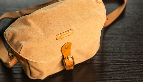 Tan leather messenger bag with brass buckle and shoulder strap on dark surface.