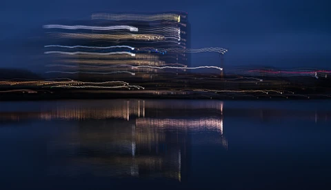 Modern building with illuminated windows reflected in still water at twilight.