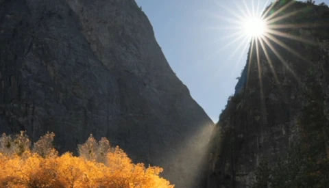 Sun streaming through a narrow mountain valley with golden autumn vegetation in the foreground and steep granite cliffs on both sides.